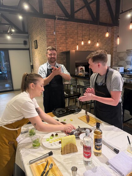 A cooking demonstration with three people, kitchen equipment, and ingredients on a table. 3