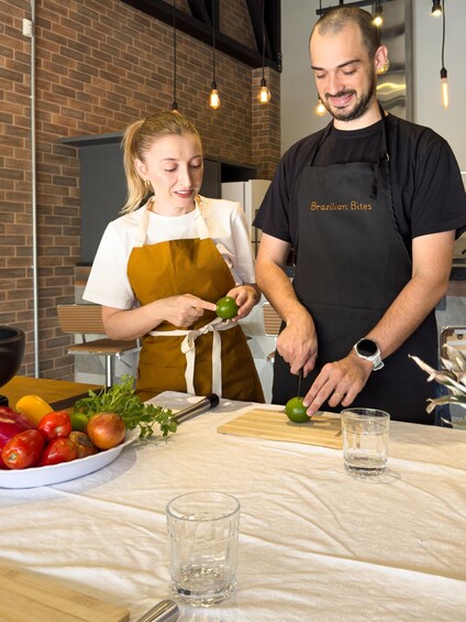 Two people preparing food, one slicing a lime, with a bowl of vegetables and a cutting board on the table. 5