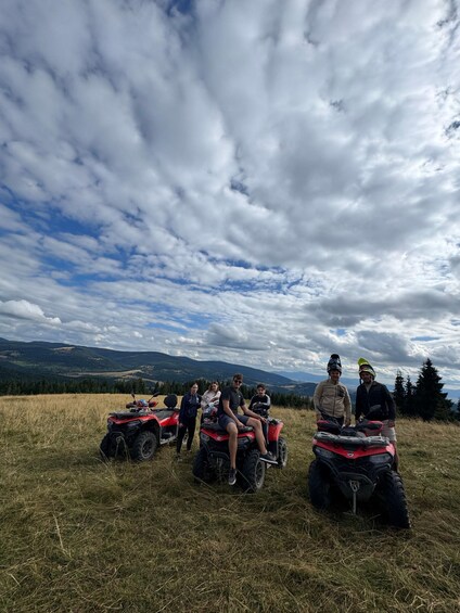 A group of people on quad bikes in a grassy field with mountains in the background. 3