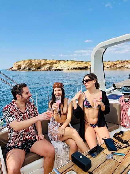 Three people on a boat with drinks, rocky cliffs in the background. 3