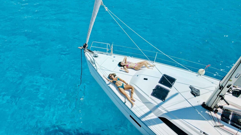 Two people sunbathing on a sailboat in clear blue waters. 1