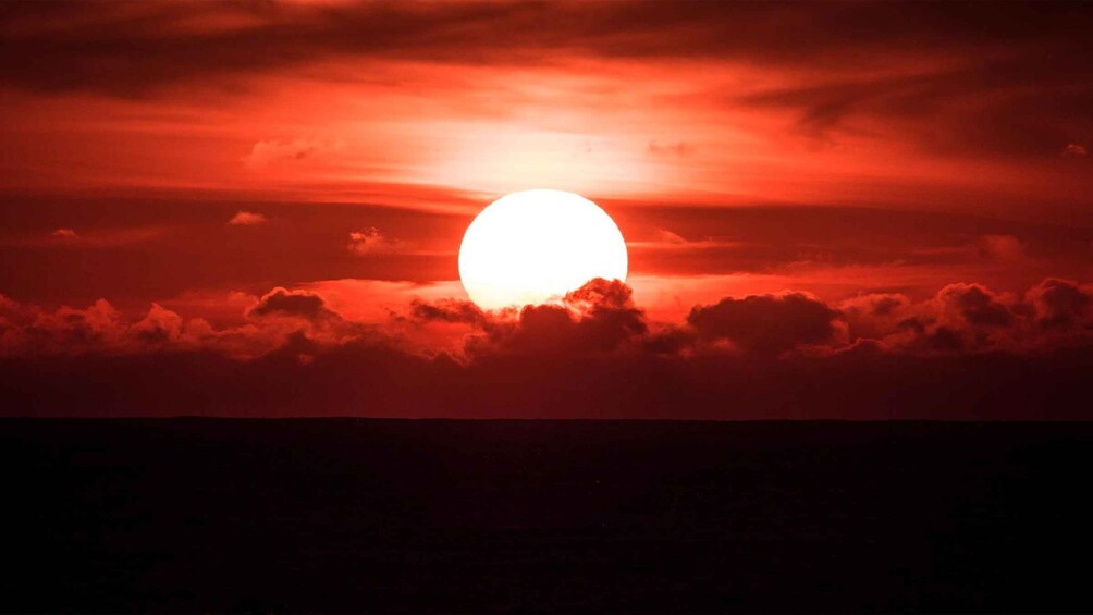 A sunset with a large sun partially obscured by clouds. 2