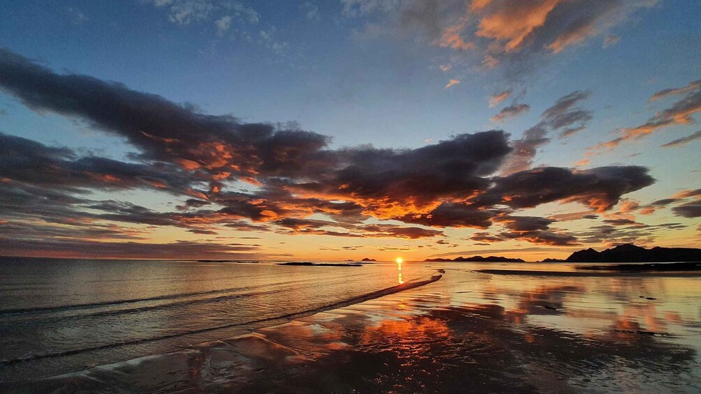 A sunset over a beach with a calm sea and a distant mountain range. 4