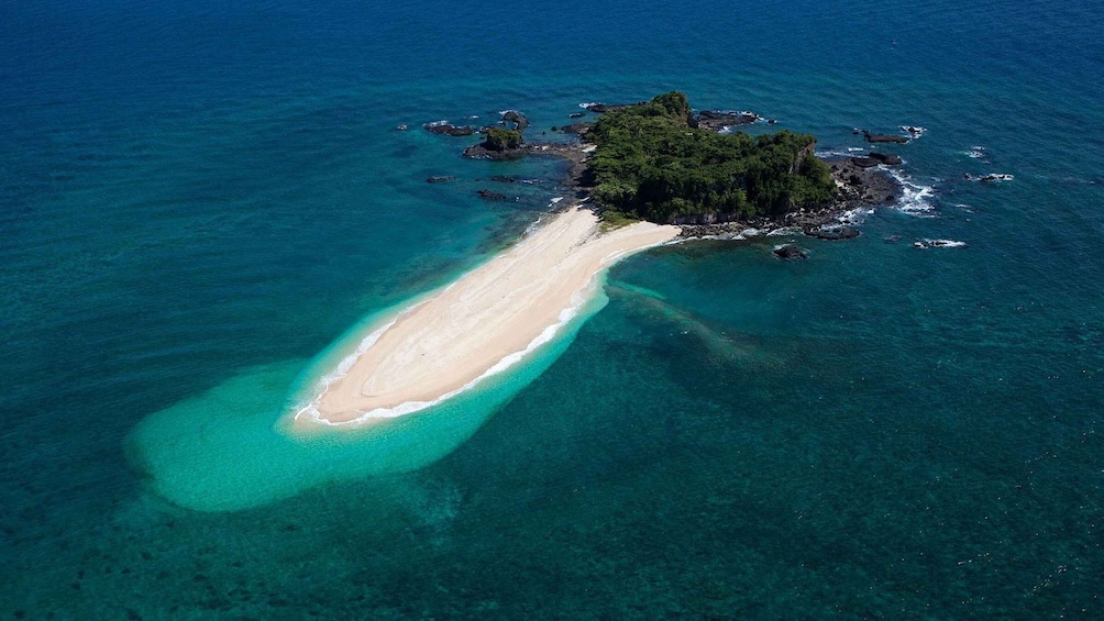 An aerial view of a narrow, elongated island with a sandy beach and clear turquoise waters. 1