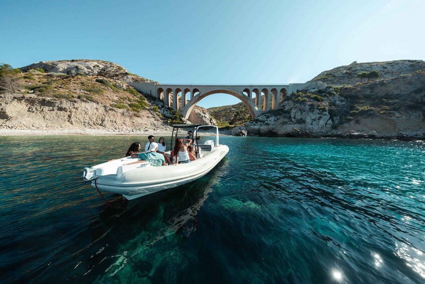 A boat on clear turquoise water with a stone bridge in the background. 1