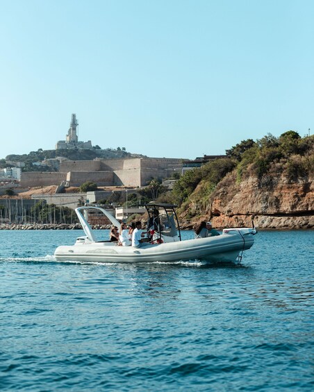 A boat with passengers on a calm body of water, a rocky coastline, and a historic building in the background. 5