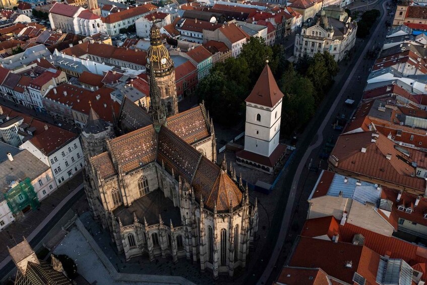 An aerial view of a historic city center with a prominent cathedral, a clock tower, and a mix of red-roofed buildings. 5