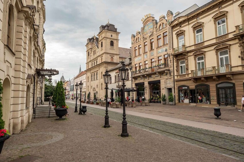 A cobblestone street lined with historic buildings, a tram track, and outdoor seating areas. 2