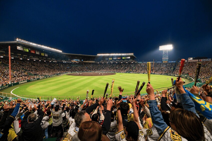A baseball stadium filled with spectators holding bats. 3