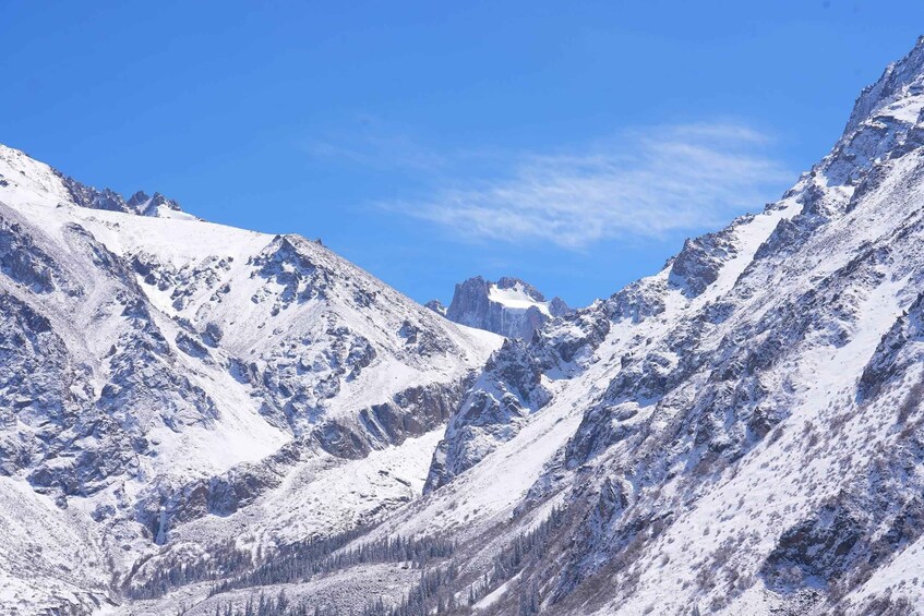 Snow-covered mountain peaks, a clear blue sky, and a distant rocky outcrop. 1