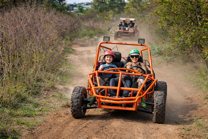 Two people in a dune buggy on a dirt path with vegetation on either side. 4