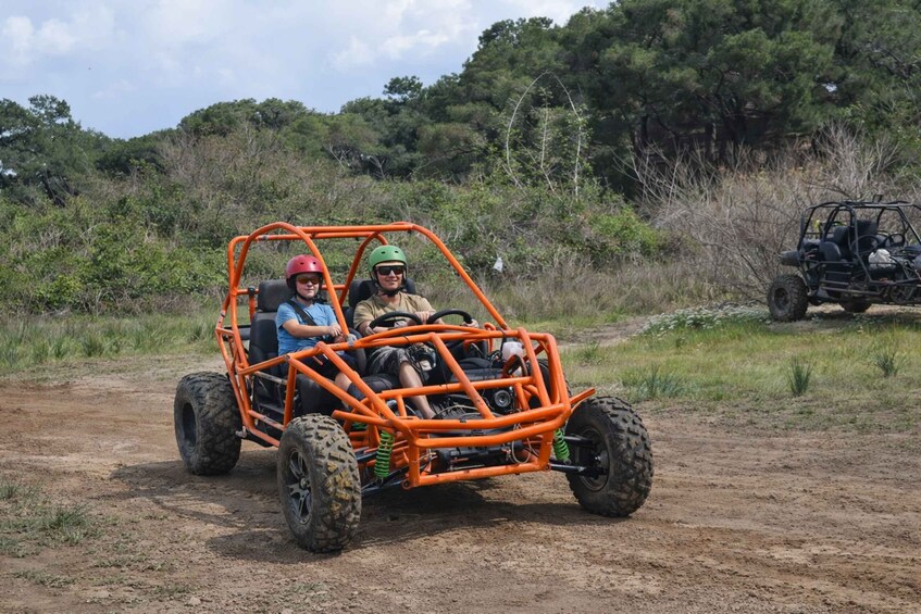 Two people in an orange off-road vehicle on a dirt path with trees in the background. 2