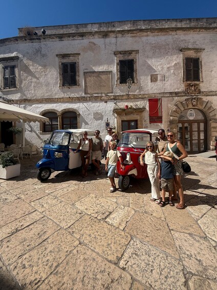 A group of people standing in front of a historic building with a red car parked nearby. 5