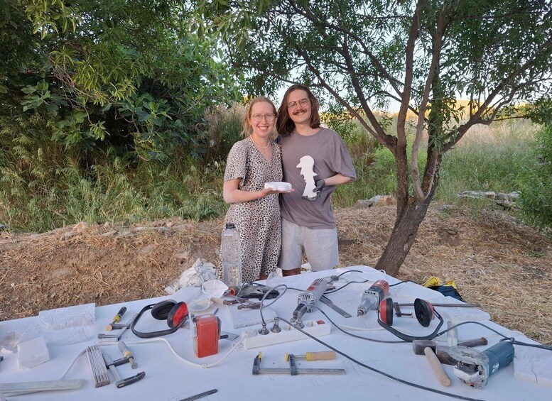 Two people standing by a table with tools and a sculpture. 5