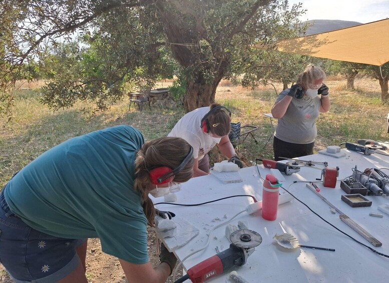 Three people working outdoors with tools and a table, surrounded by trees and a clear sky. 2