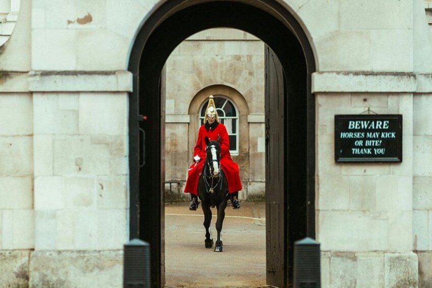 A person in a red coat riding a horse through an archway. 5