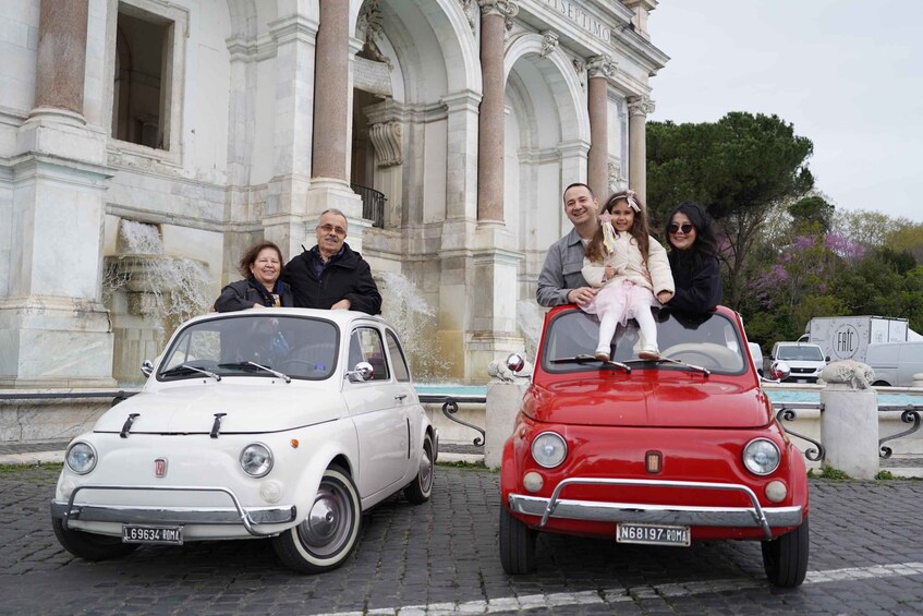 A white and a red vintage Fiat car parked in front of a classical building with columns. 2