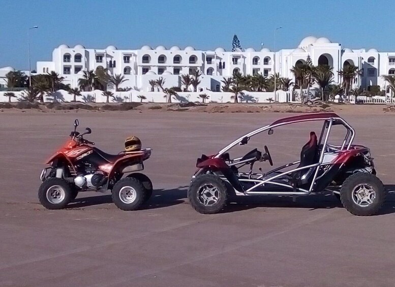 Two off-road vehicles parked in a sandy area with a white building and palm trees in the background. 2