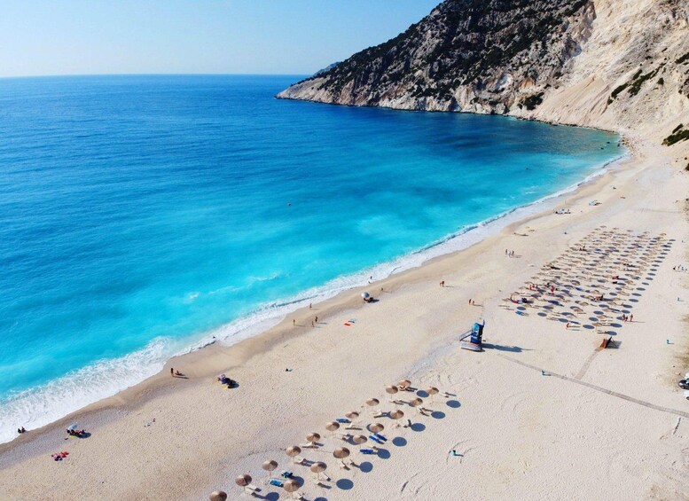 A beach with clear blue waters, sandy shore, and a rocky cliff. 5