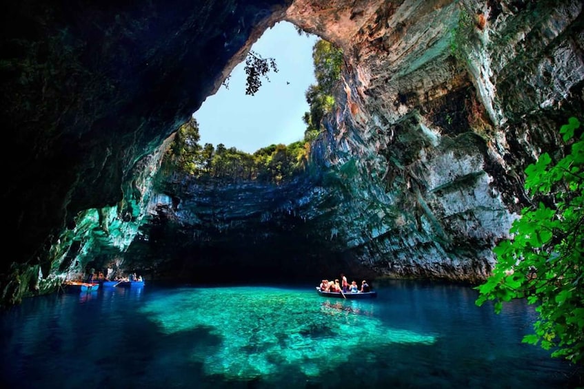 A cave opening with clear water, a boat with people, and surrounding greenery. 2