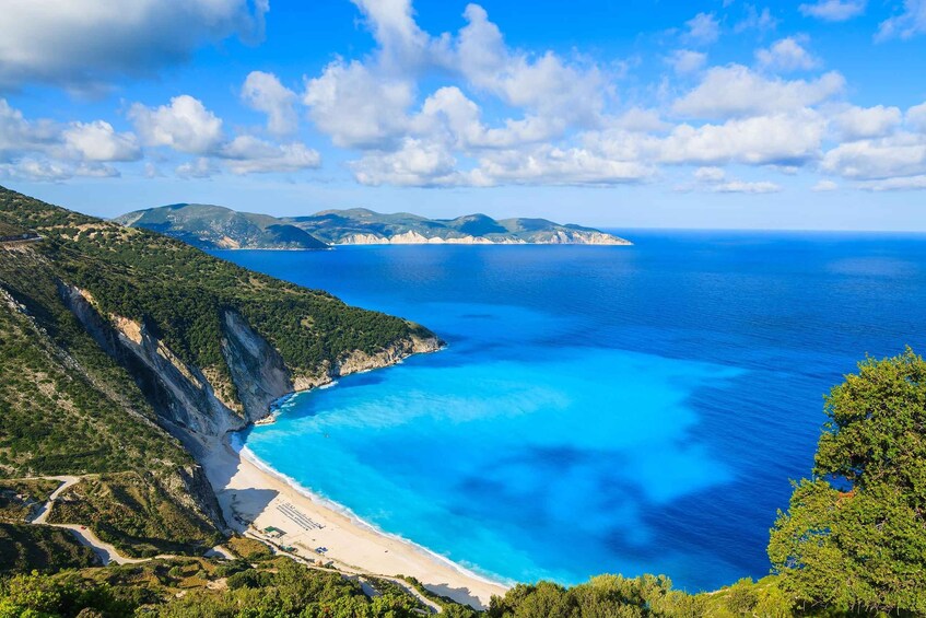 A coastal landscape with a clear blue sea, a sandy beach, and green hills. 1