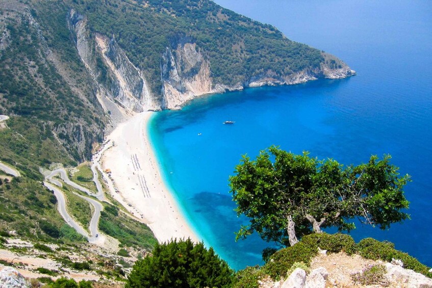 A coastal landscape with a winding road, a sandy beach, and a clear blue sea. 4