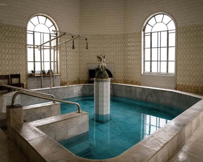 An indoor swimming pool with arched windows and a statue in the center. 1