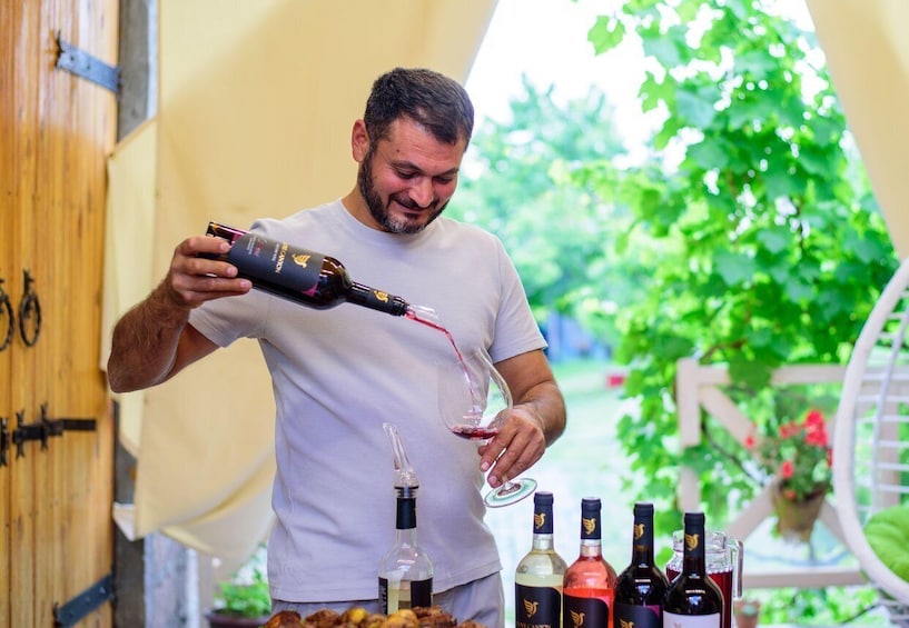 A person pouring wine into a glass, surrounded by wine bottles. 1