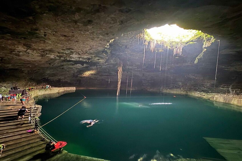A cave with a pool of water, wooden steps, and people around. 2