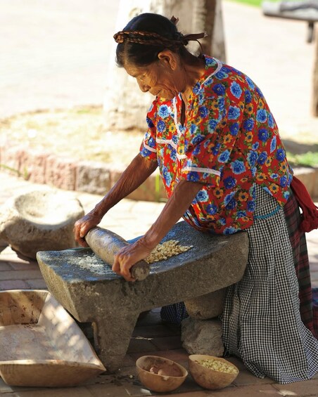 An elderly woman grinding corn using a stone mill. 1