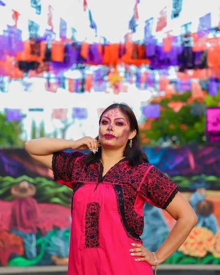 A person in a pink dress with black lace details, standing in front of a colorful mural with abstract designs. 2