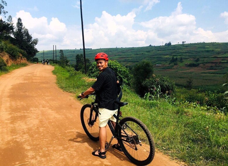 A person on a dirt road with a bicycle, surrounded by green hills and a clear sky. 1