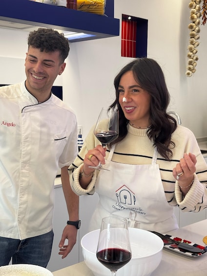 Two people in a kitchen, one wearing a chef's uniform and the other in casual attire, holding wine glasses. 4