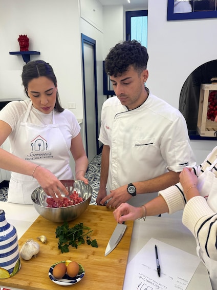 Two people in a kitchen preparing food, with ingredients like garlic, eggs, and parsley on the counter. 5