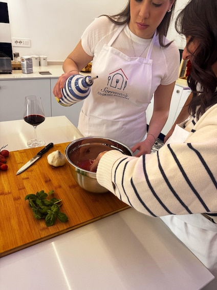 A person in a white apron with a logo, pouring a liquid from a blue and white container into a mixing bowl on a wooden cutting board. 2