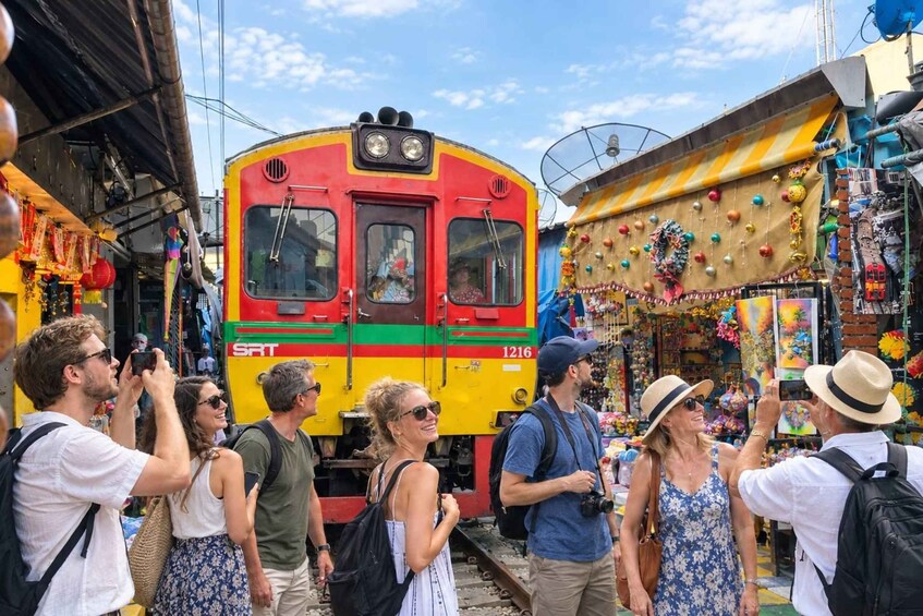 Een kleurrijke trein met nummer 1216, omringd door mensen die foto's maken en een markt met diverse koopwaar. 5
