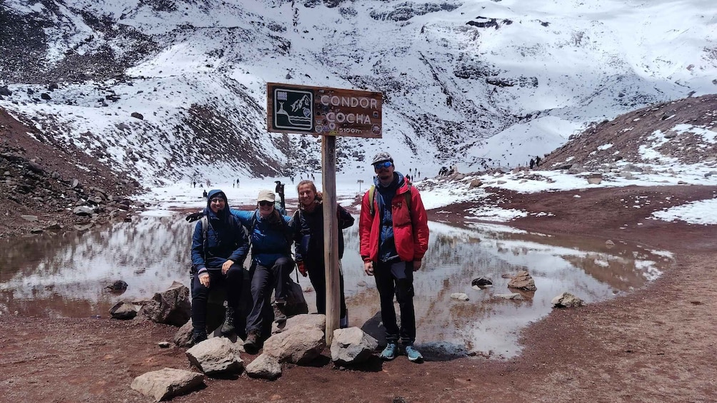 A group of hikers at a mountain trailhead with a sign indicating 'CONDOR COCHA' and a distance of 5100m. 5