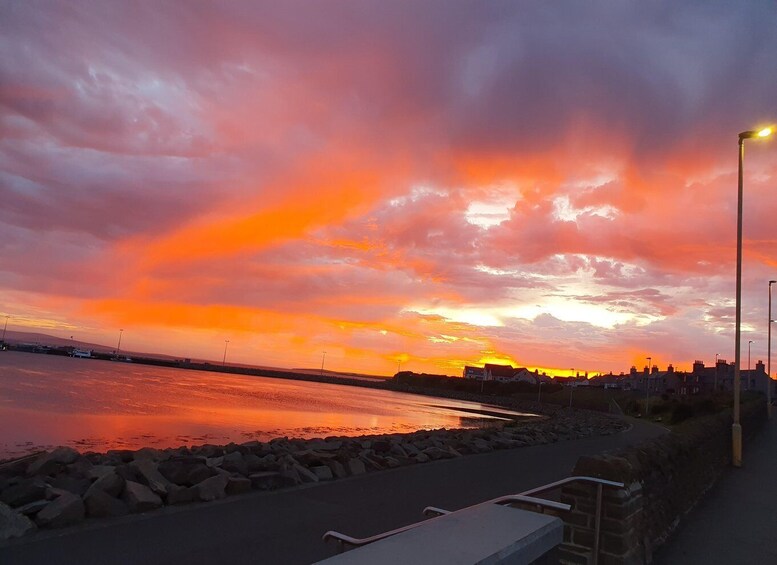 A sunset over a body of water with a rocky shoreline and a row of houses in the background. 5