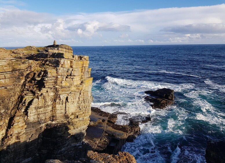 A coastal cliff with layered rock formations and the ocean waves crashing against the base. 4