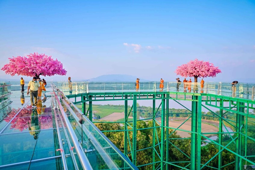 A glass bridge with pink cherry blossom trees, a clear sky, and a river in the background. 4