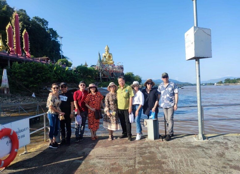 A group of people standing by a river with a golden statue in the background. 1