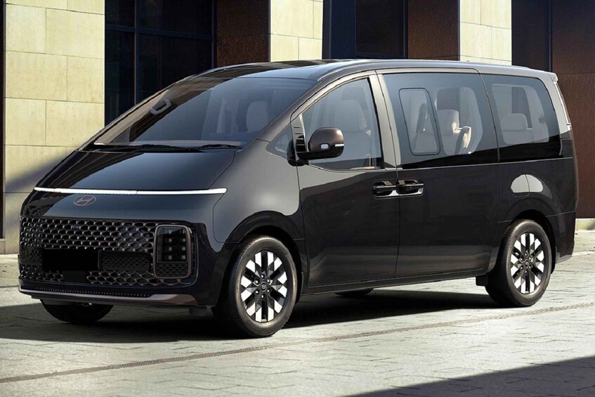 A black minivan parked in front of a building with large windows and a tiled facade. 4