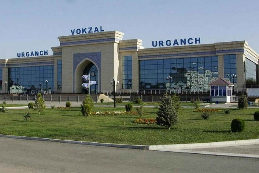 A modern building with 'VOKZAL URGANCH' signage, surrounded by a well-maintained lawn and a clear sky. 5