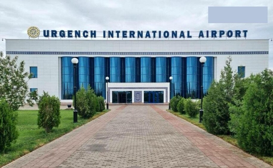 Urgench International Airport with a prominent entrance, large blue windows, and a clear sky. 2