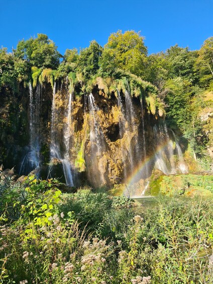 A waterfall cascading down a rocky cliff surrounded by lush greenery. 2