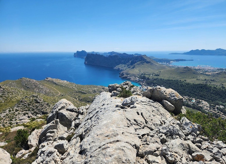 A rocky coastline with a clear blue sea, distant mountains, and a small settlement. 4