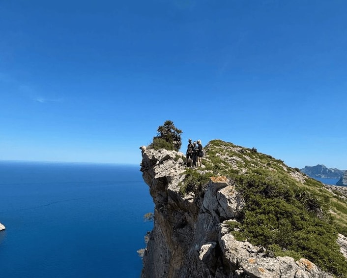 A rocky cliff with a group of people standing on top, overlooking a vast body of water. 1