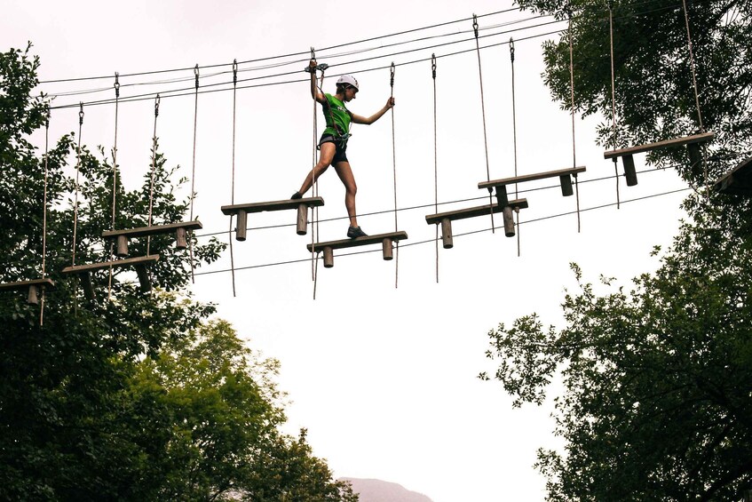 A person navigating an outdoor obstacle course with wooden platforms and ropes. 2