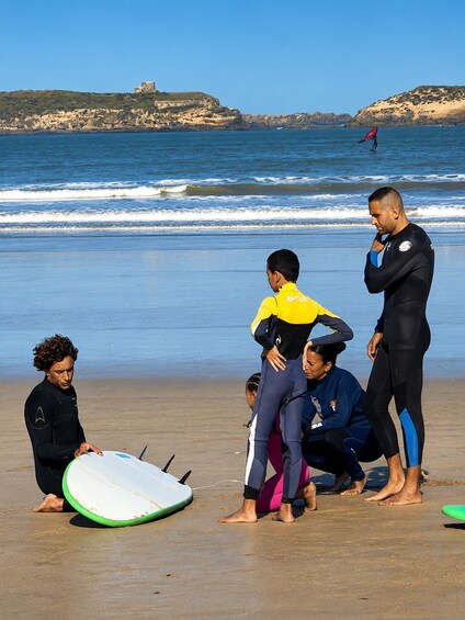 A beach scene with people in wetsuits, a surfboard, and a rocky coastline in the background. 2