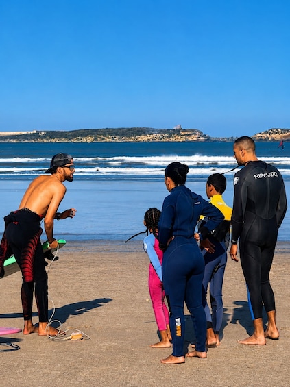 A group of people on a beach, some wearing wetsuits, with ocean waves in the background. 3